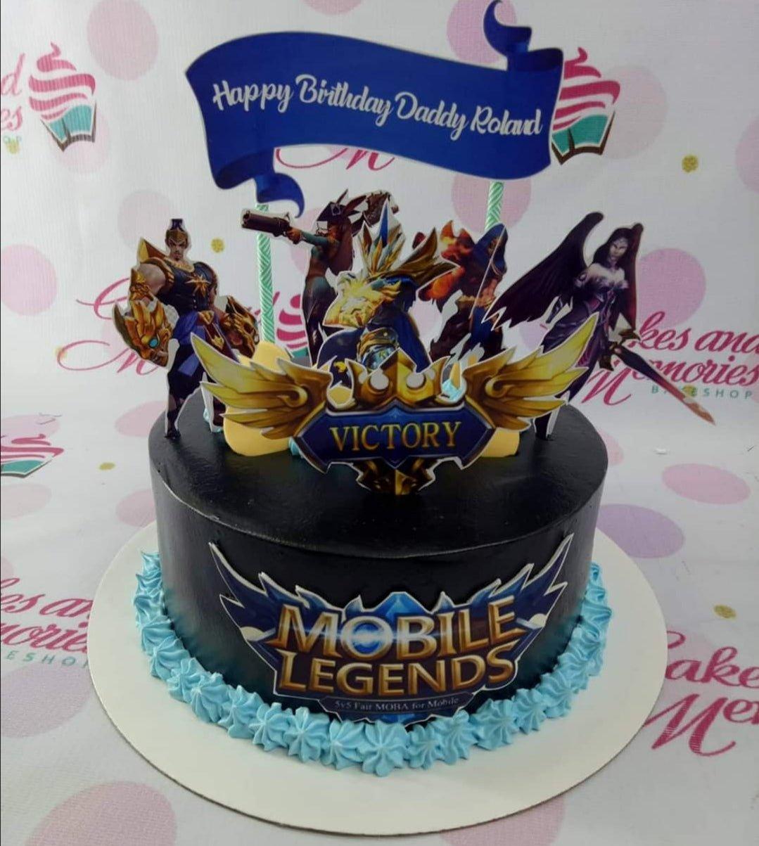 Mobile Legends themed birthday cake with black icing, blue piped borders, and character printouts for Daddy Roland.