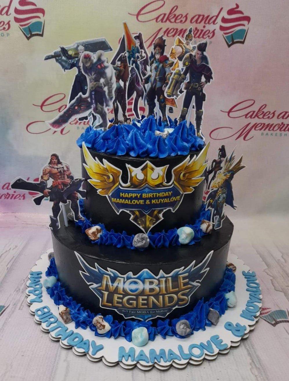 Two-tier black Mobile Legends themed birthday cake with blue icing borders and character printouts.