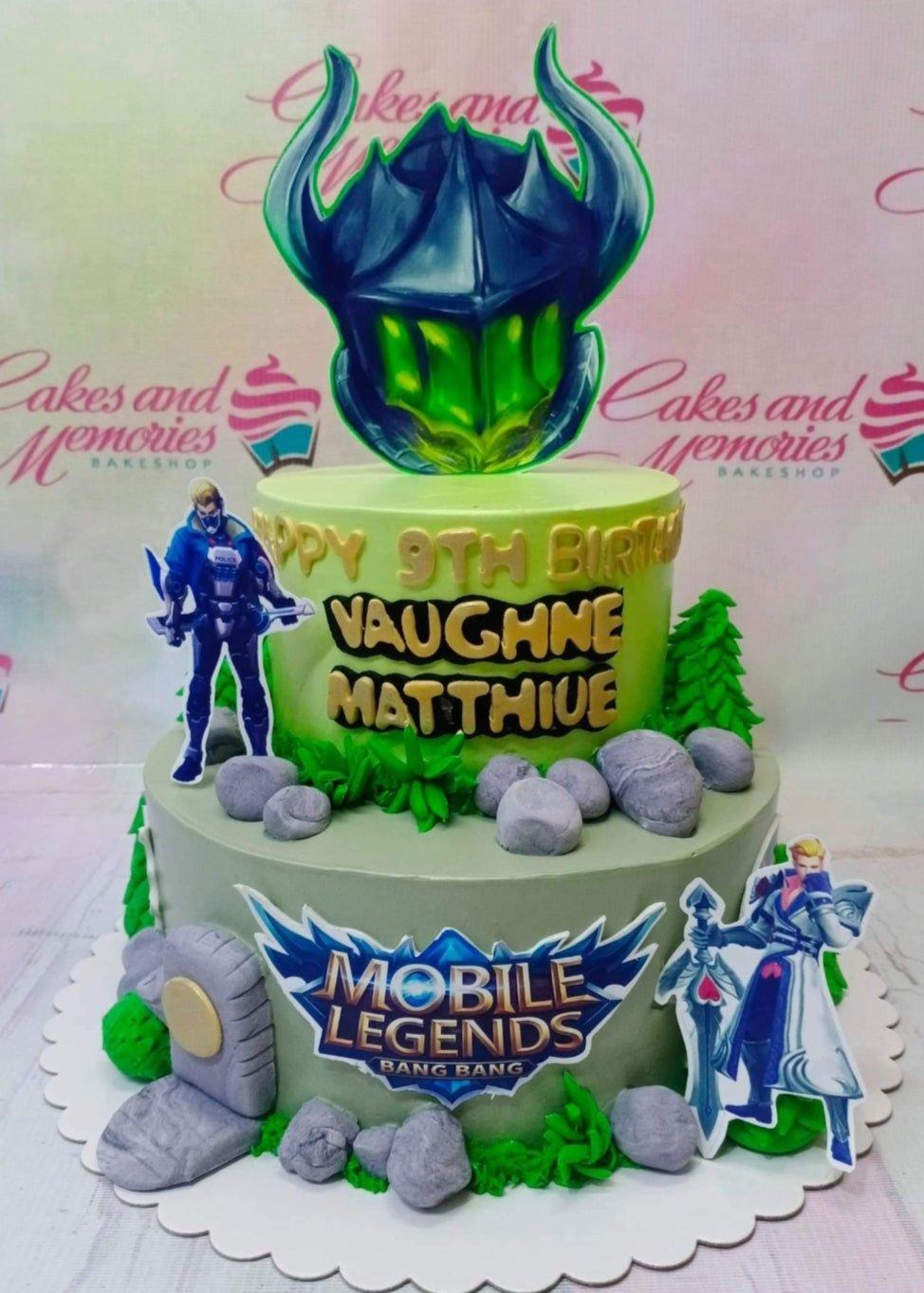 Two-tier Mobile Legends themed birthday cake in green and gray with character printouts and fondant rock decorations.