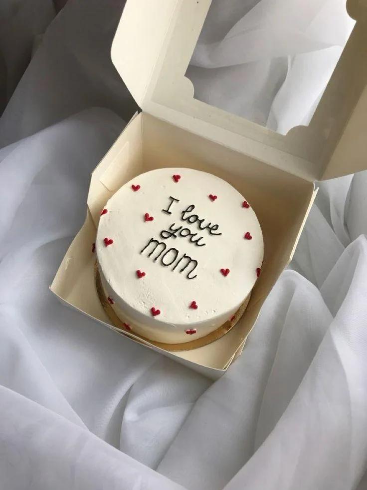 White minimalist bento cake with red icing hearts and a handwritten message saying I love you mom.