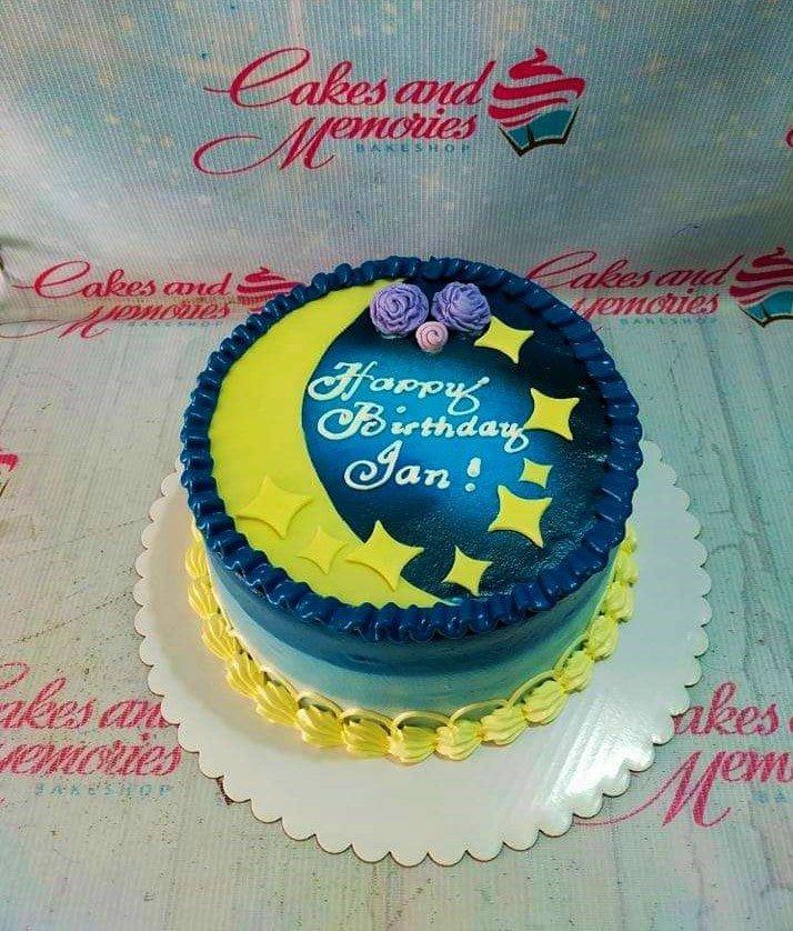 Blue and yellow moon and stars themed birthday cake with purple icing flowers and a personalized message.