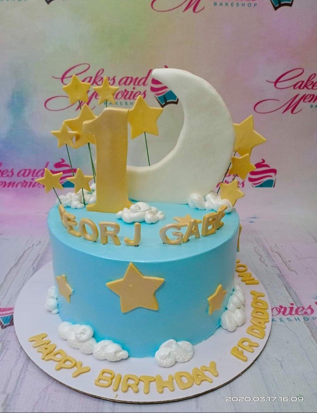Light blue 1-tier birthday cake with a large white crescent moon, gold number one, and yellow stars with white icing clouds.