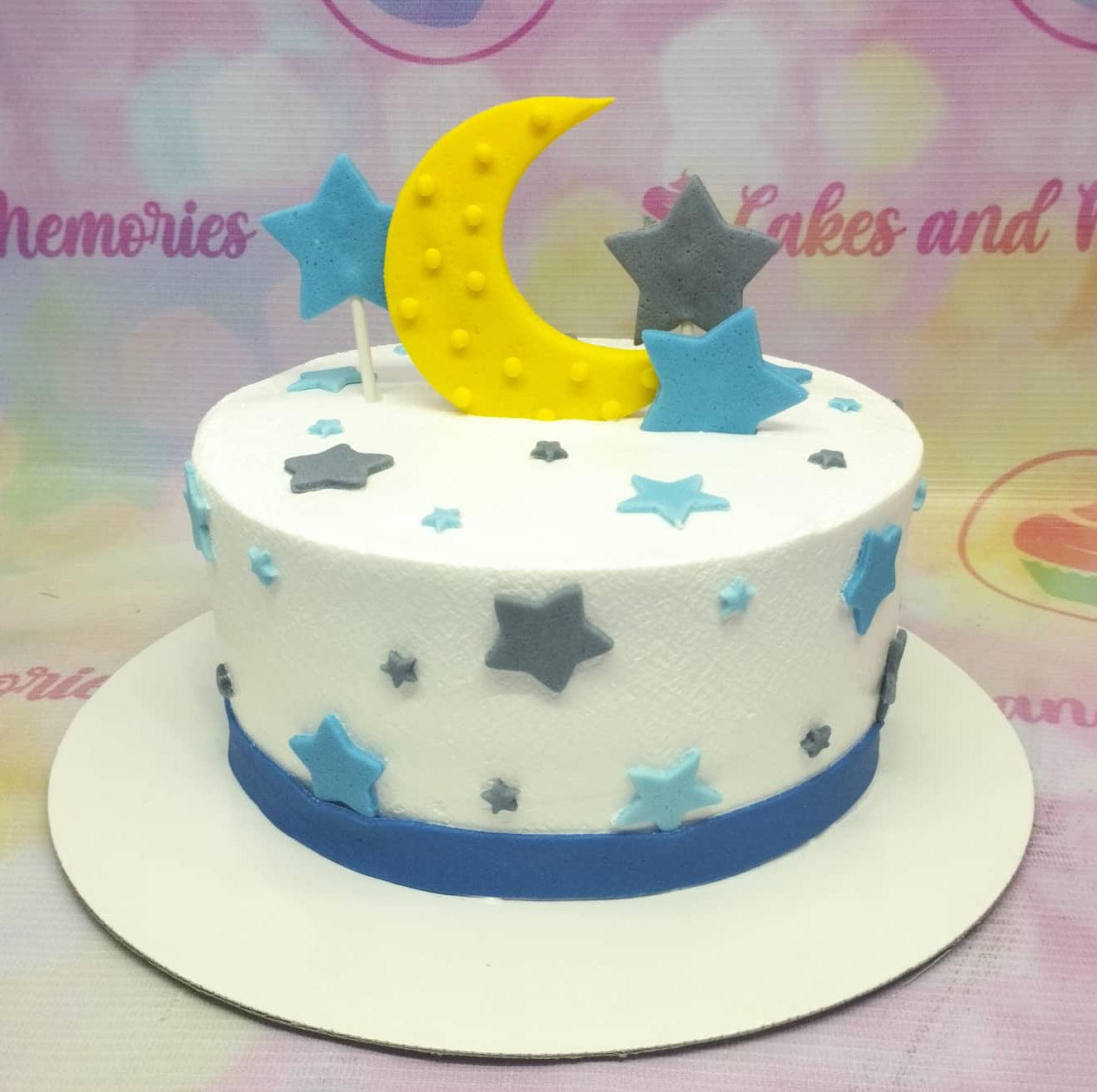 White round cake decorated with blue and gray fondant stars and a large yellow crescent moon topper.