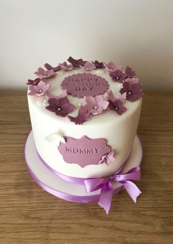 White fondant cake for Mother's Day decorated with purple and pink gumpaste flowers and butterflies with a 'Happy Mothers Day' plaque.