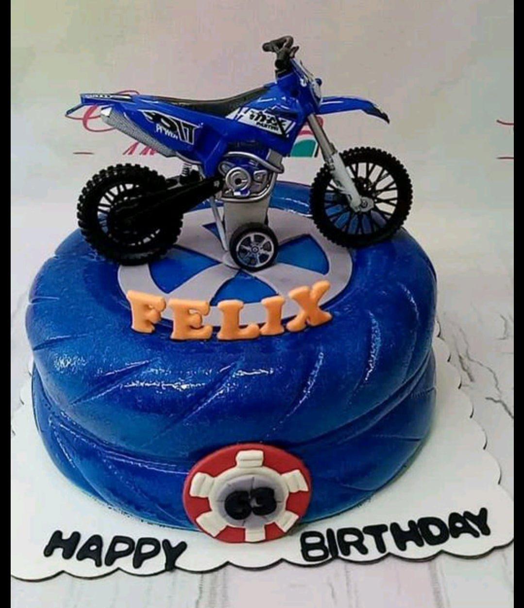 Blue tire-shaped fondant cake with a blue toy motocross bike topper and orange gumpaste name letters.