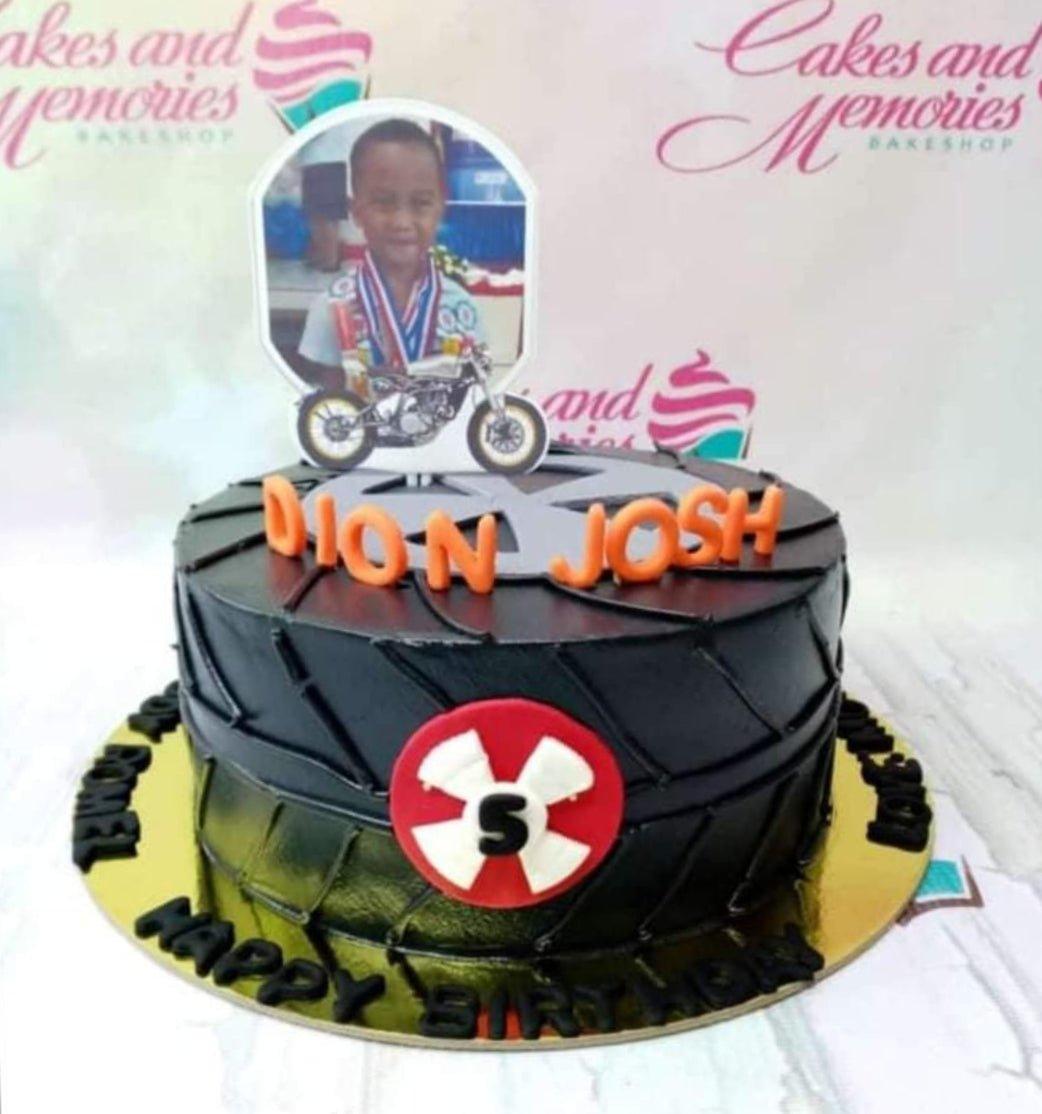 Black tire-themed birthday cake with a motorcycle printout and a photo topper for Dion Josh.