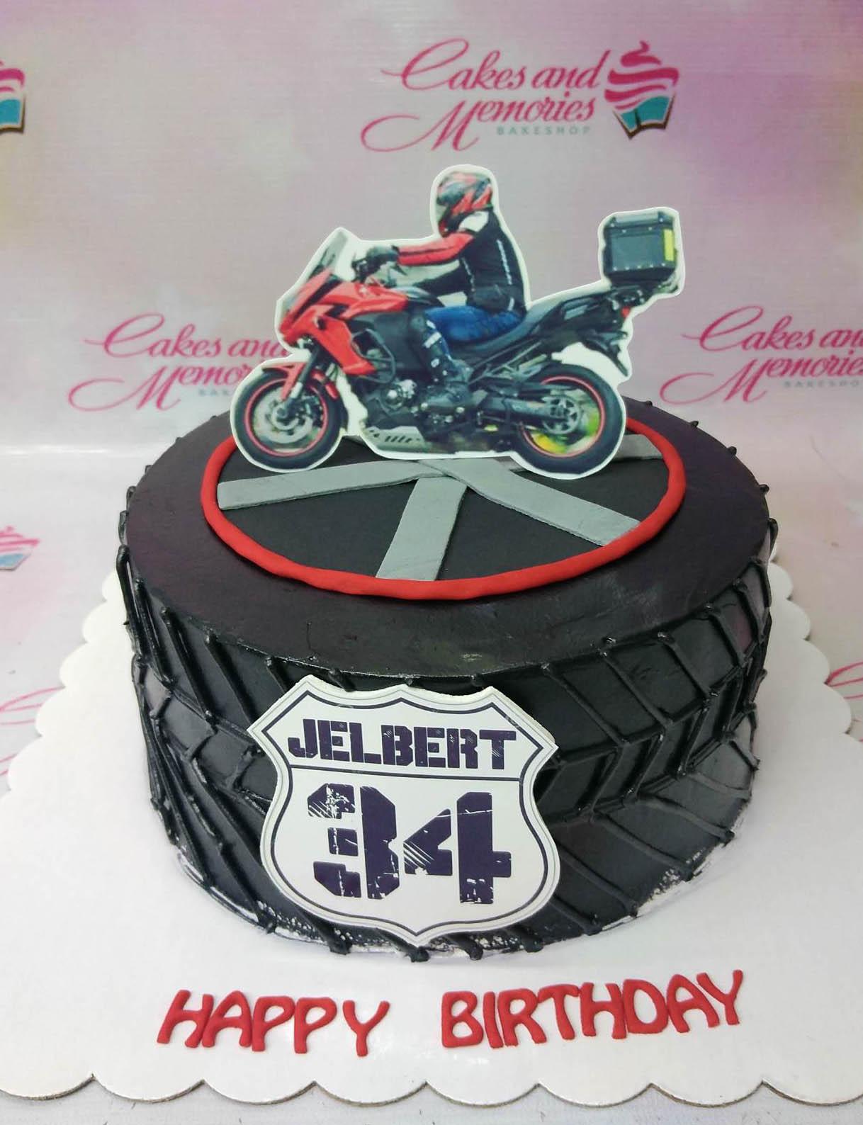 Black tire-themed birthday cake with a motorcycle rider printout topper and a route sign for Jelbert's 34th birthday.