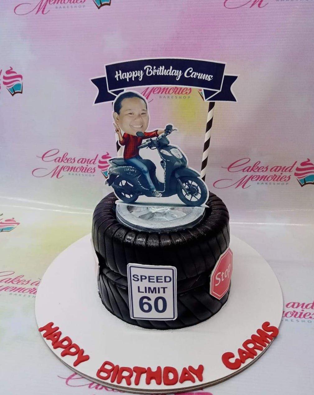 Black tire-shaped fondant cake with a motorcycle rider printout topper and road sign decorations.