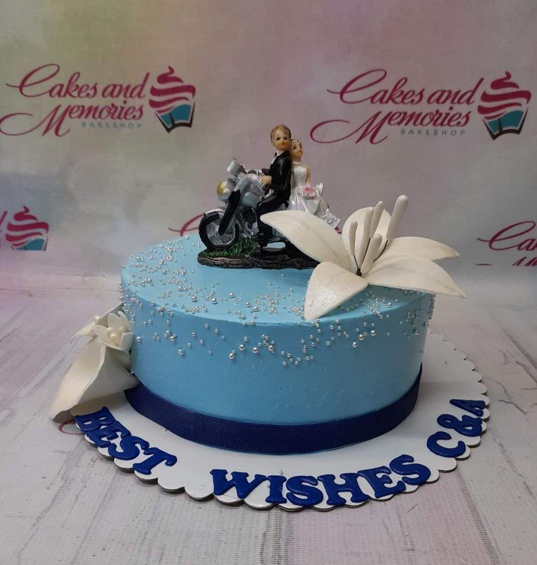 Light blue wedding cake with a motorcycle couple topper, large white lilies, and silver dragees.