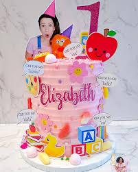 Pink 1-tier Ms Rachel birthday cake with character printouts, apple topper, and alphabet blocks