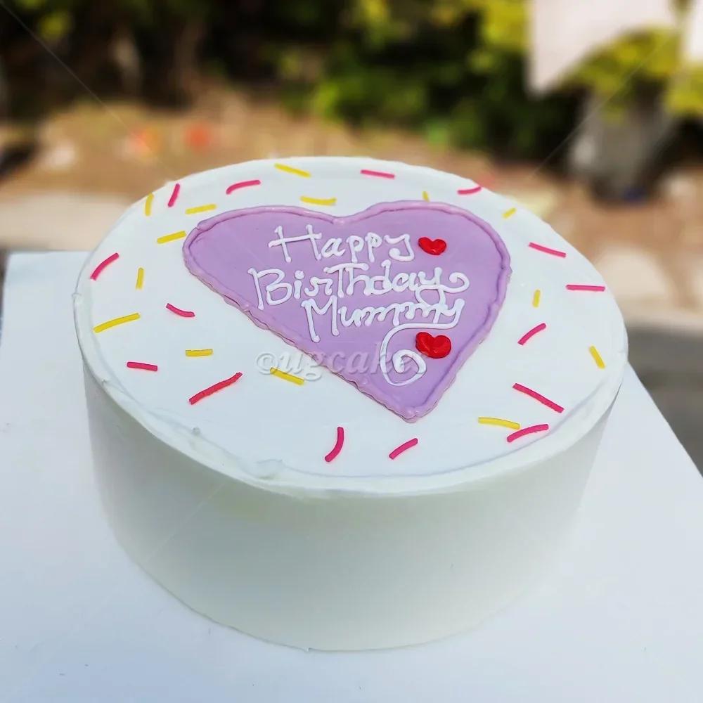 White bento cake with a purple heart center, colorful sprinkles, and 'Happy Birthday Mummy' message in white icing.