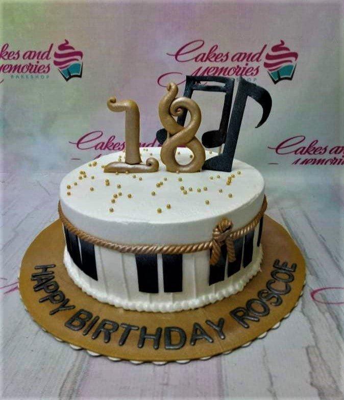 White 1-tier music themed birthday cake with gold number 18 and black musical note toppers on a gold base board.