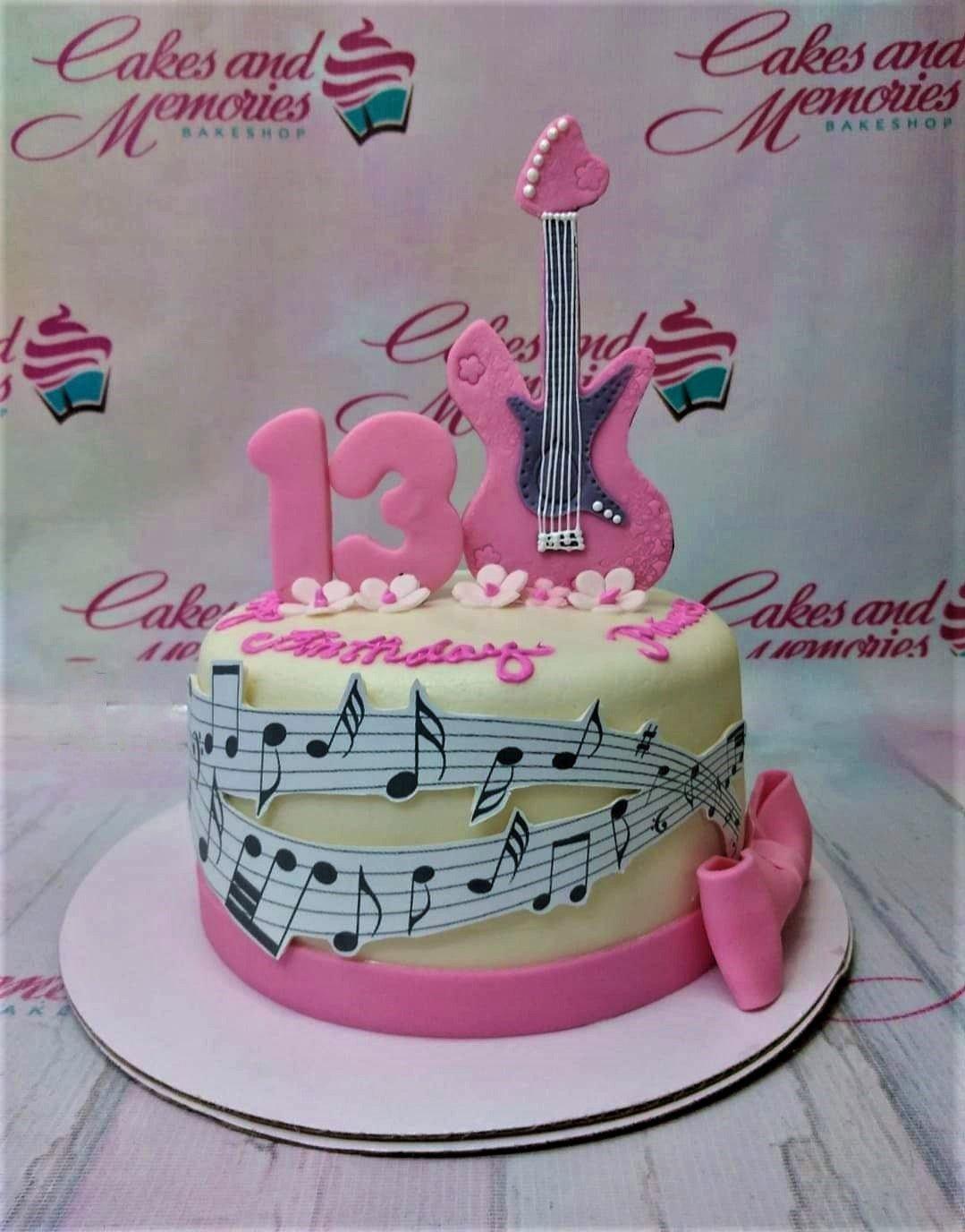 Pink and white music themed cake with a pink fondant guitar, number 13, and musical note printouts on the side.