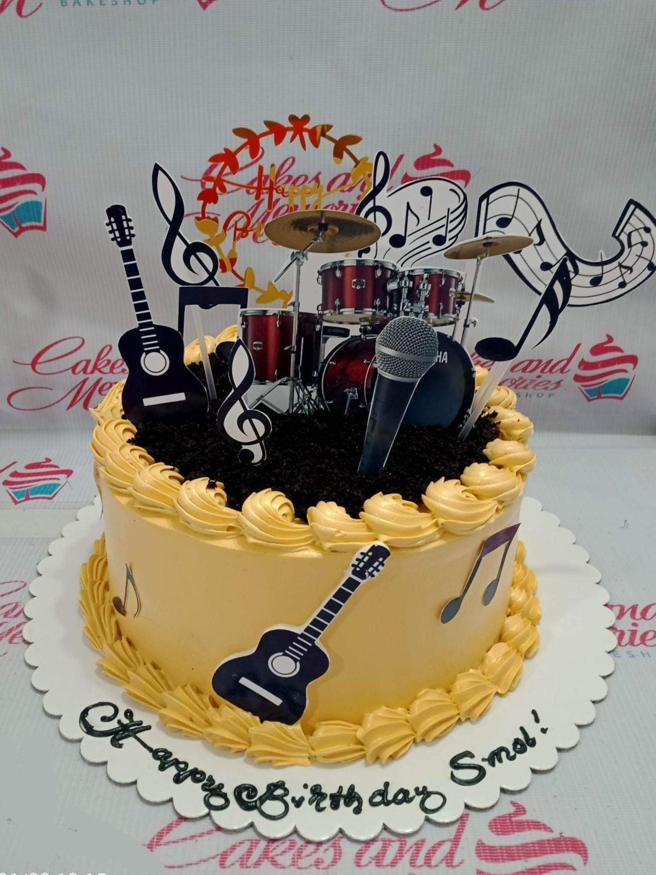 Music themed birthday cake with yellow icing, chocolate cookie crumbs, and various musical instrument printout toppers including drums and guitars.
