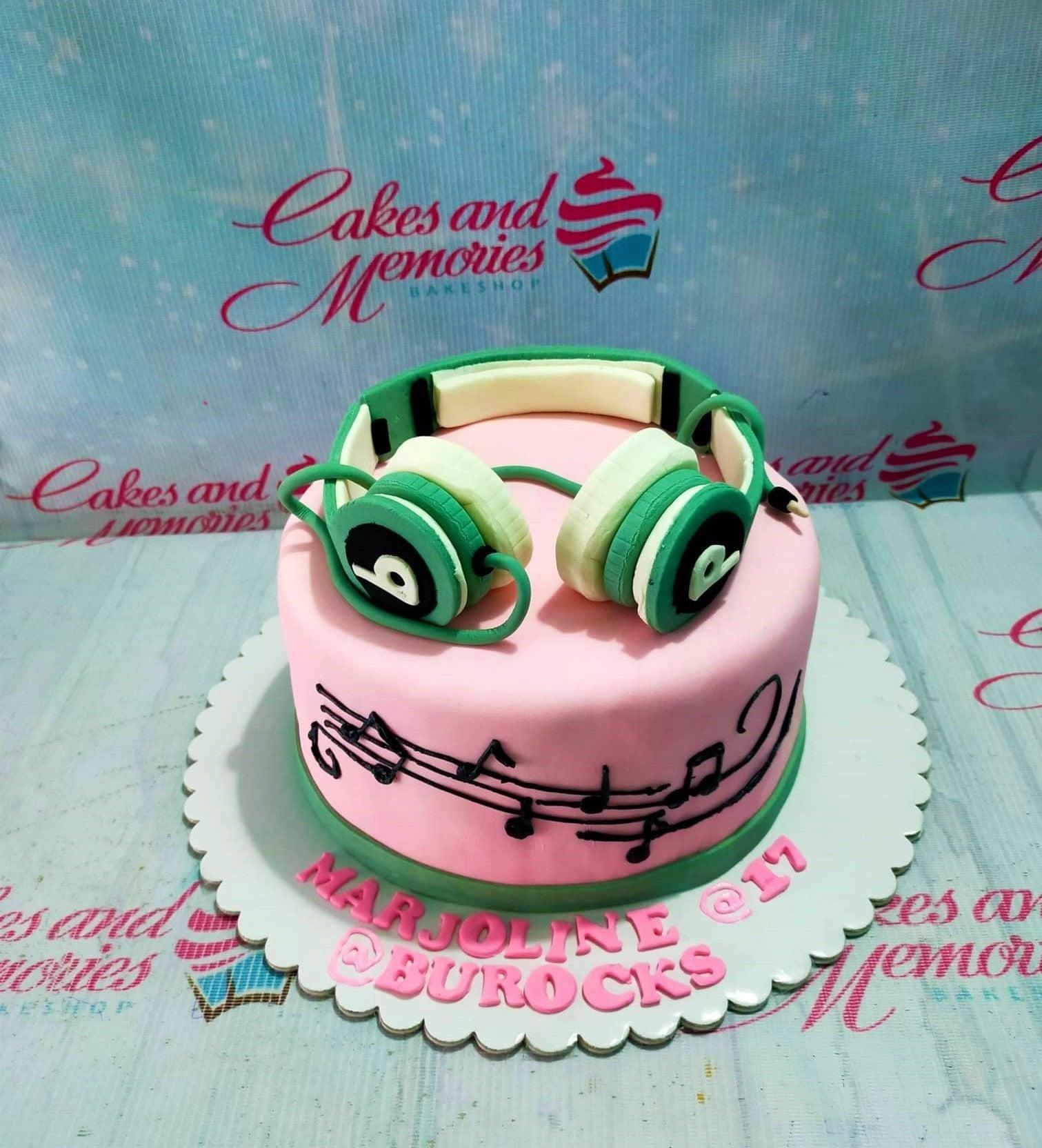 Pink fondant cake with green headphones topper and black musical notes on the side.