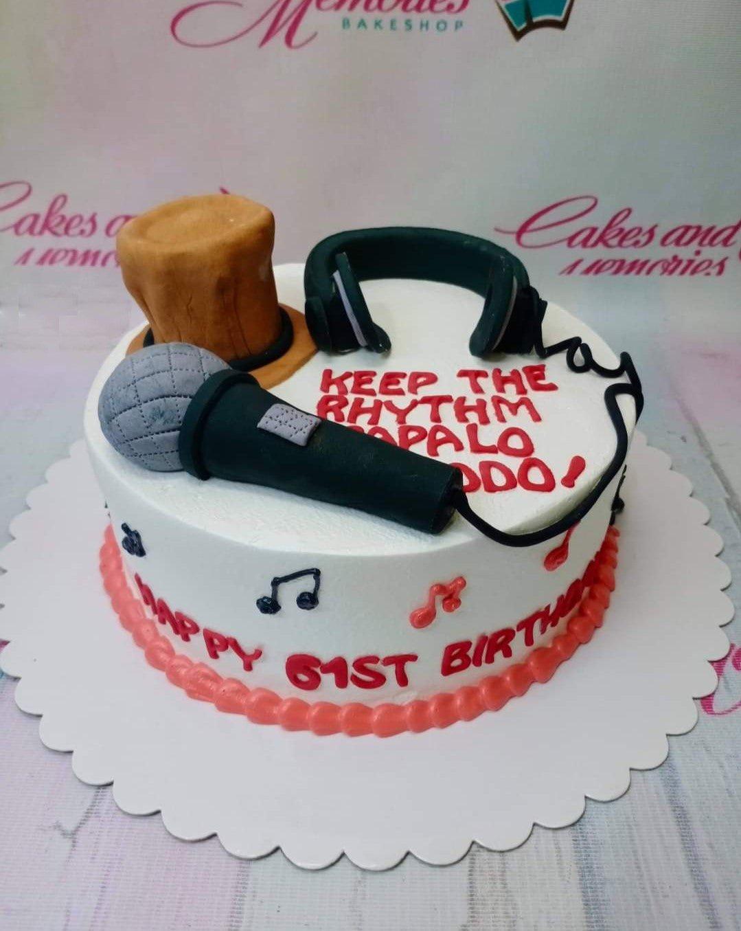 White round birthday cake with a fondant microphone, headphones, and a brown top hat, decorated with red and black musical notes.