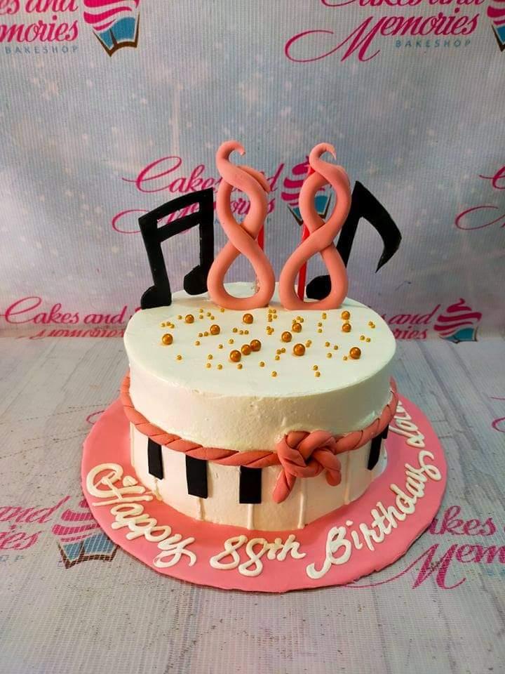 White 1-tier music themed birthday cake with pink fondant piano keys, music notes, and gold dragees on a pink base board.
