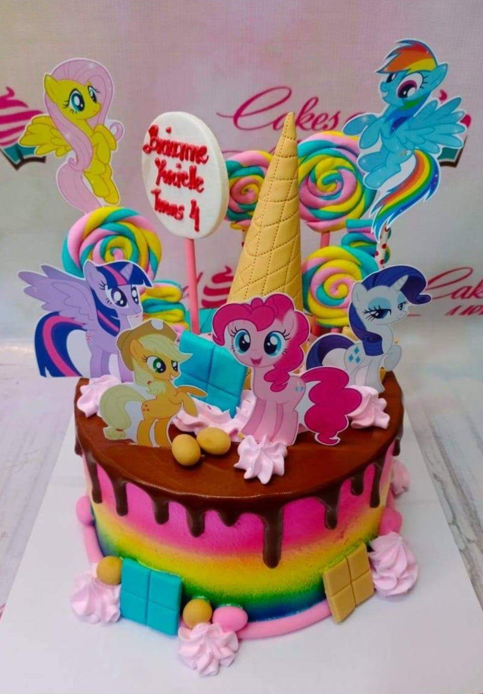 Rainbow My Little Pony birthday cake with chocolate drip, colorful lollipops, and character printouts.