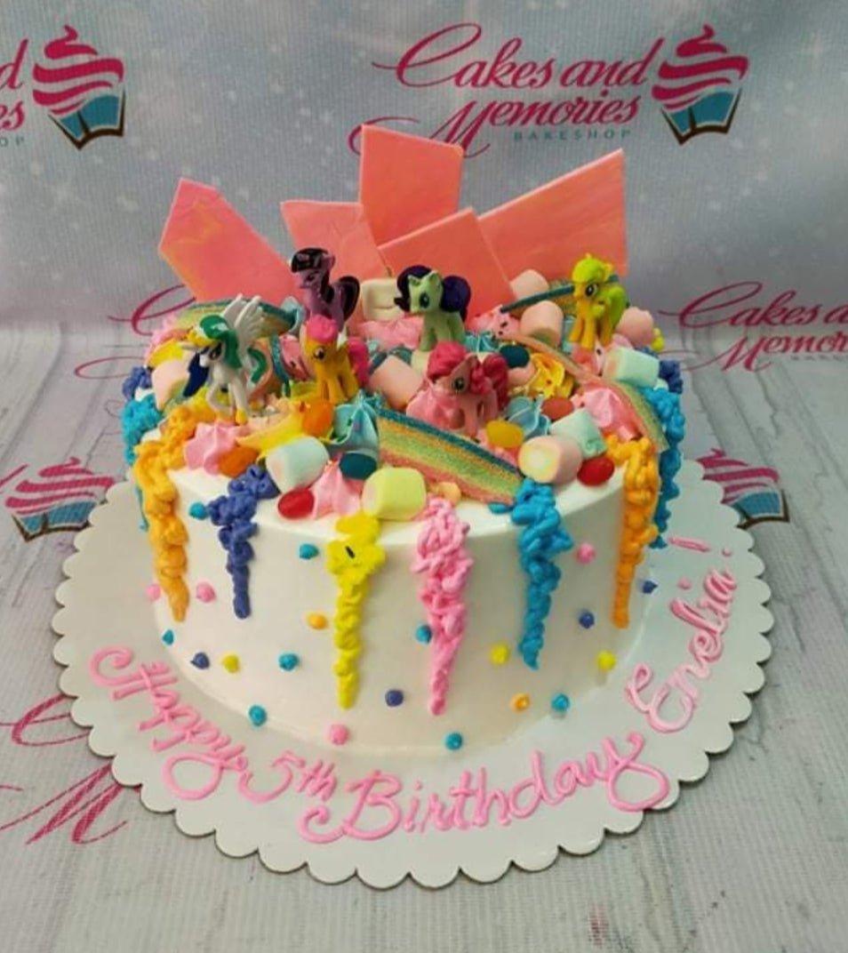 Colorful My Little Pony birthday cake with rainbow icing drips, marshmallows, and toy pony figurines.