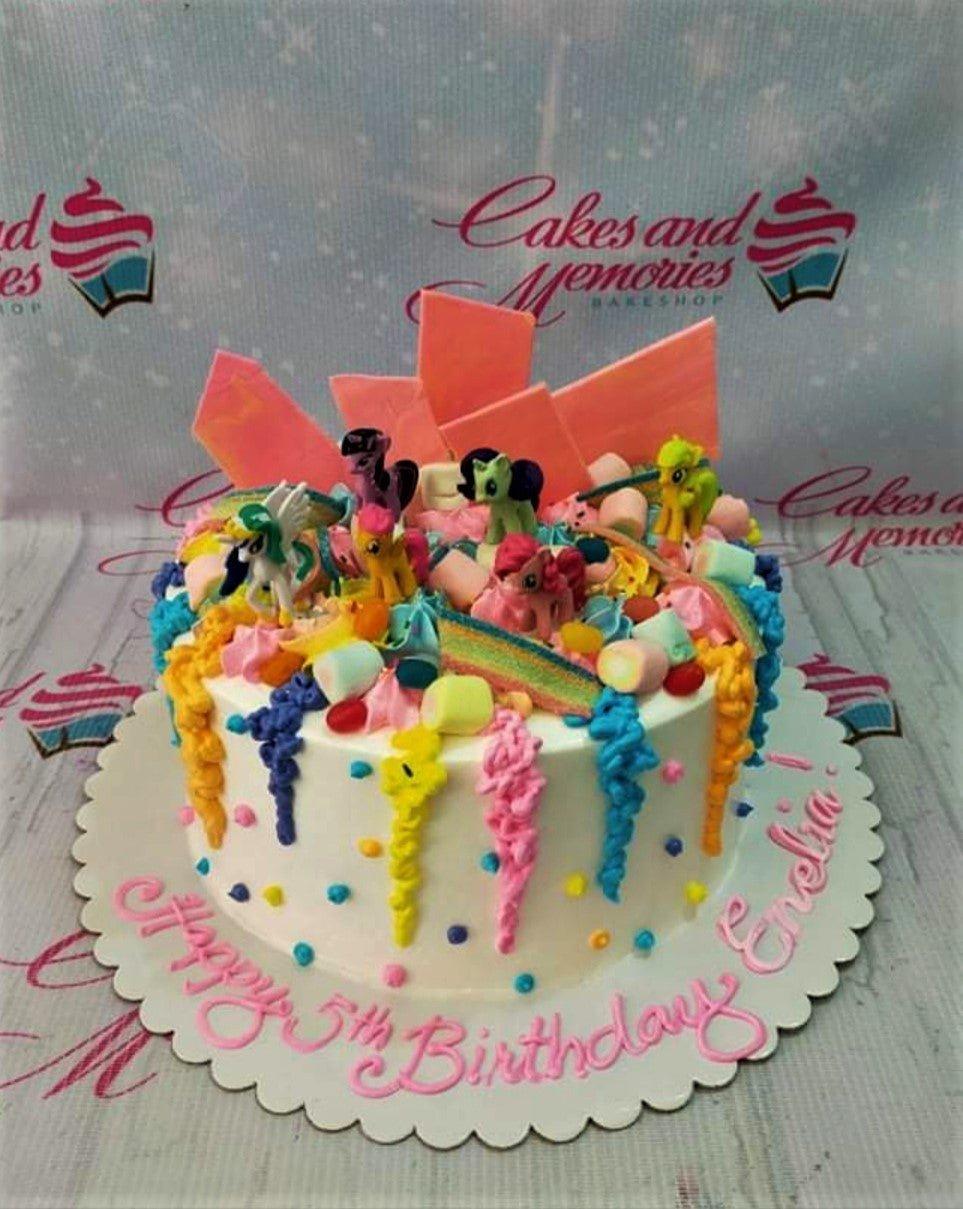Colorful My Little Pony birthday cake with rainbow icing drips, marshmallows, and candy toppers on a white base.