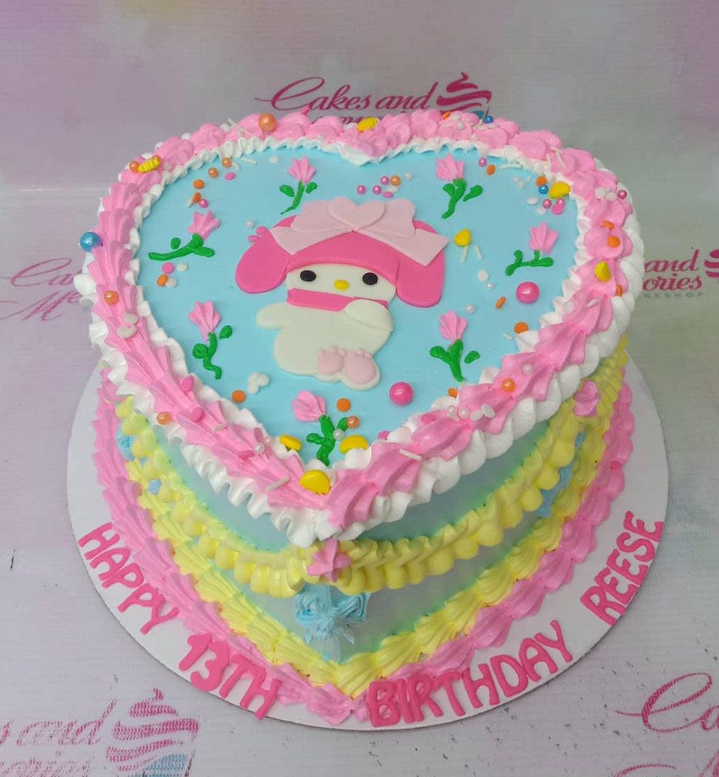 Heart-shaped light blue cake with pink and yellow icing ruffles, My Melody printout topper, and colorful sprinkles.