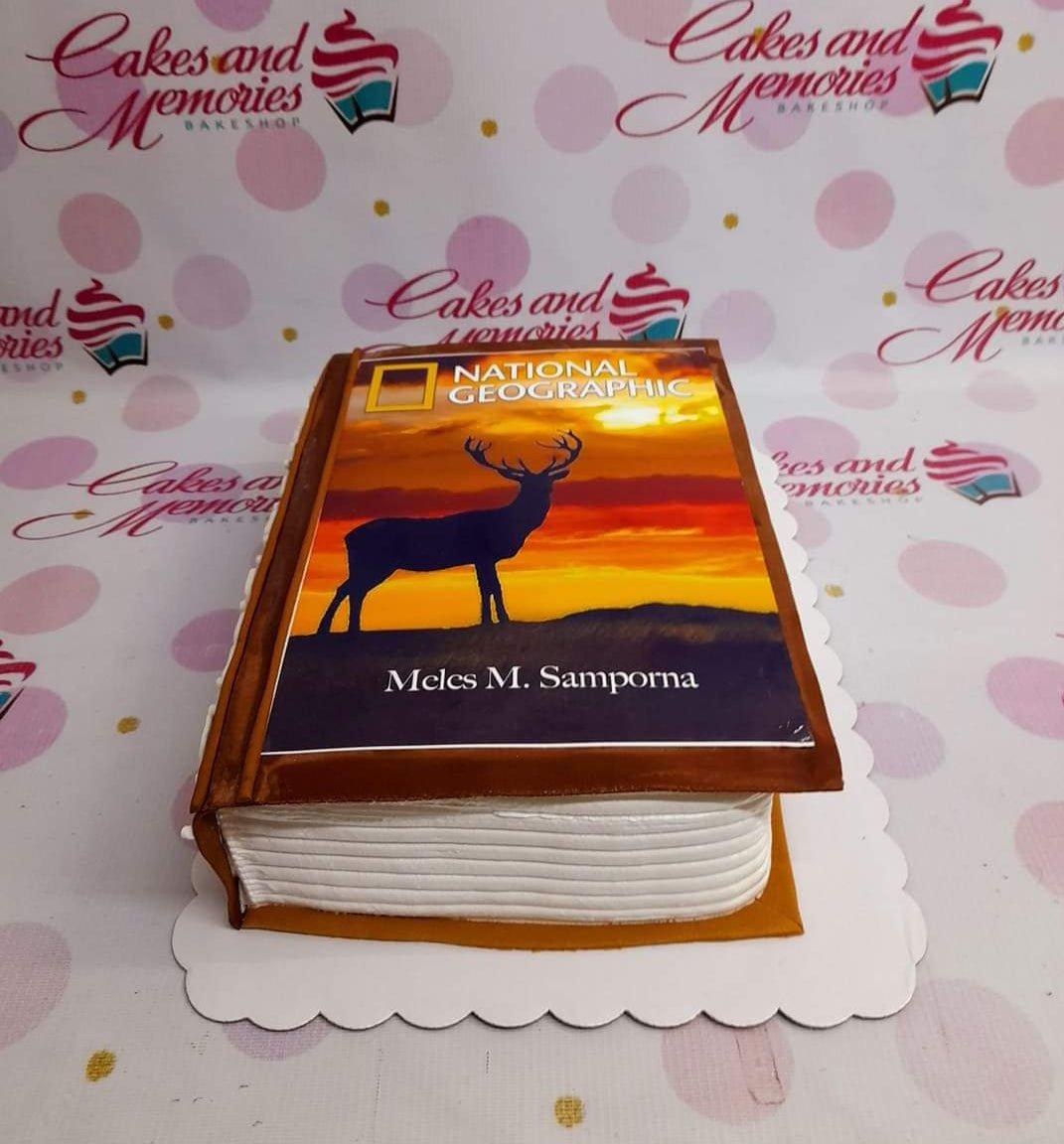 National Geographic book cake featuring a silhouette of a deer against a sunset background with personalized name text.