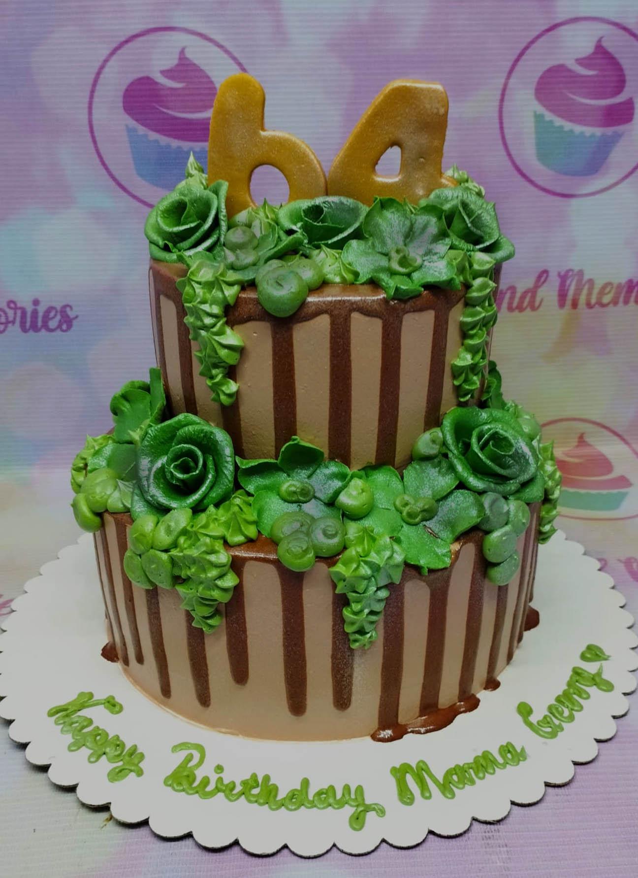 Two-tier brown cake with green icing roses and leaves, chocolate drips, and a gold number 64 topper.