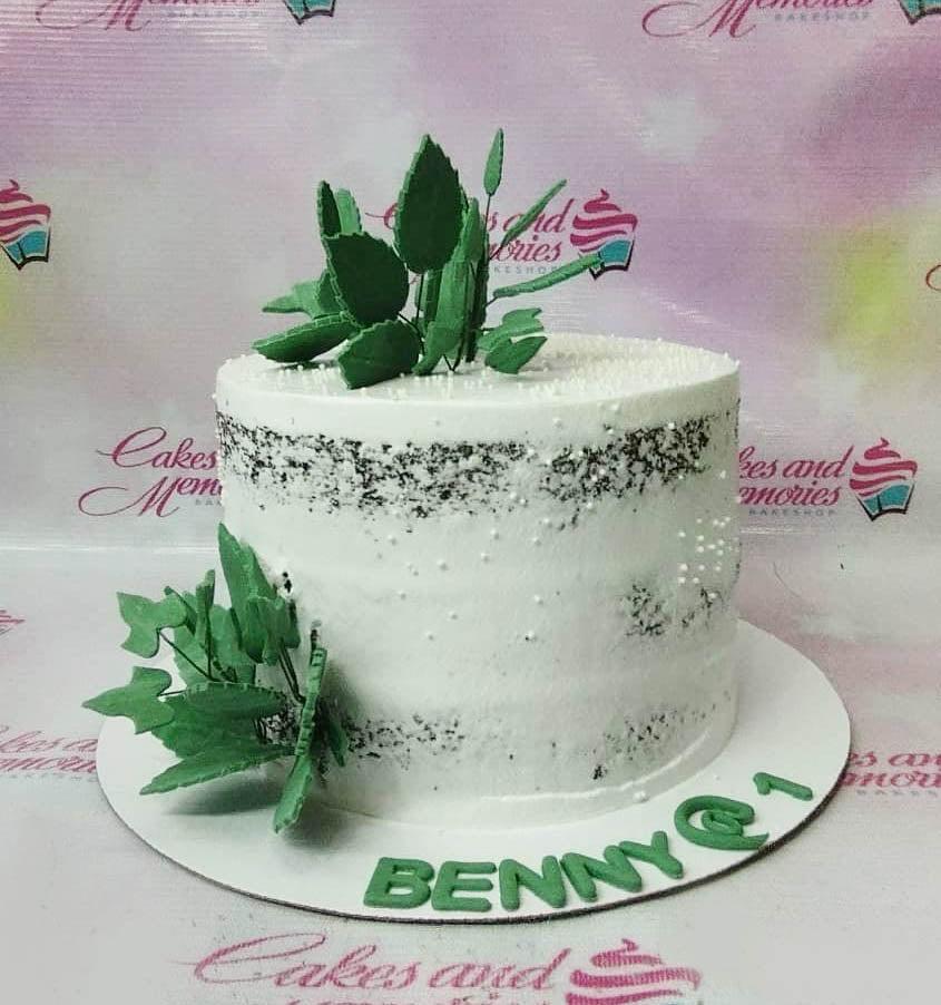 Semi-naked chocolate cake with white icing, green gumpaste leaves, and white pearl sprinkles.