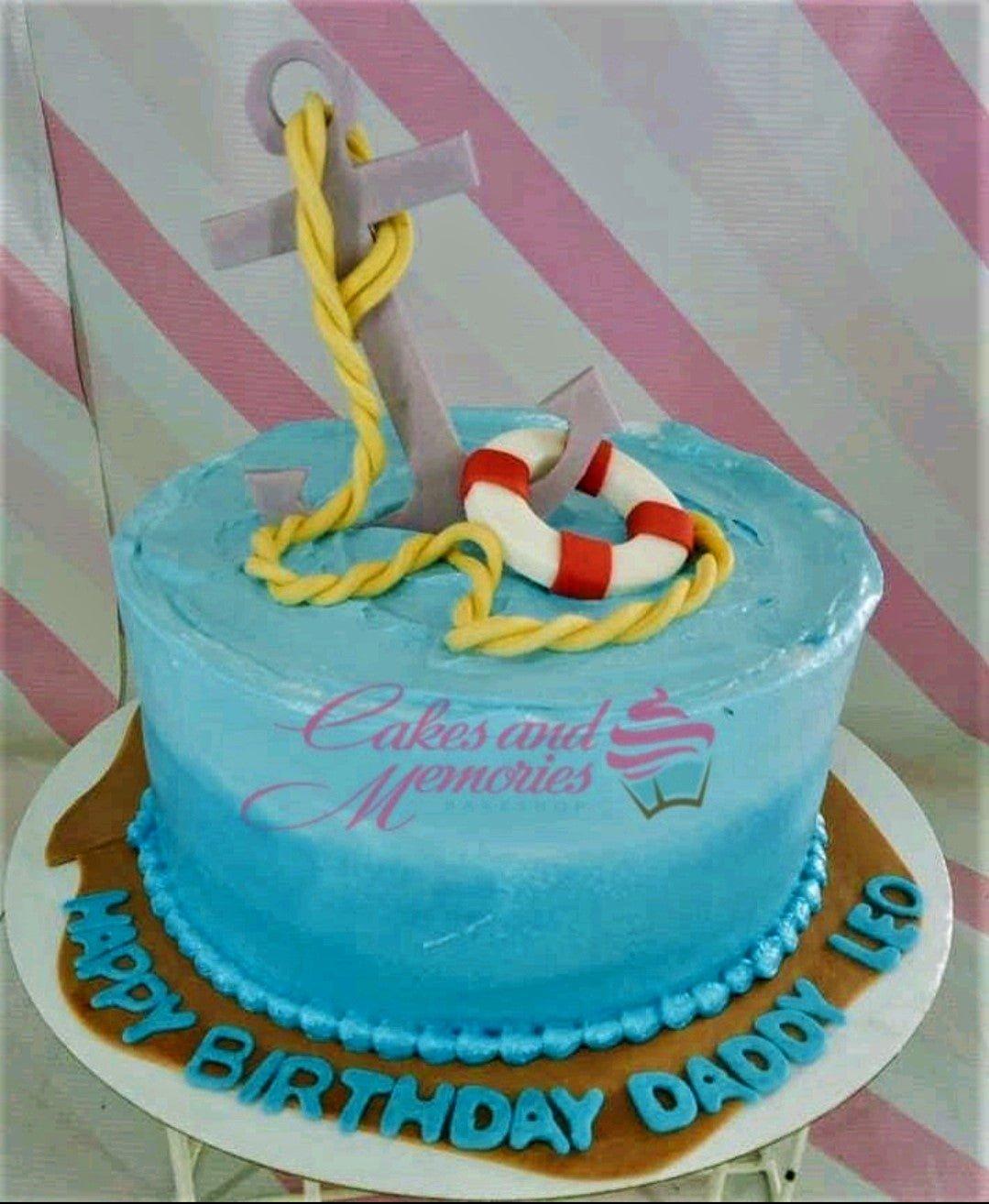 Nautical themed blue gradient birthday cake with a large anchor, lifebuoy, and rope fondant toppers.