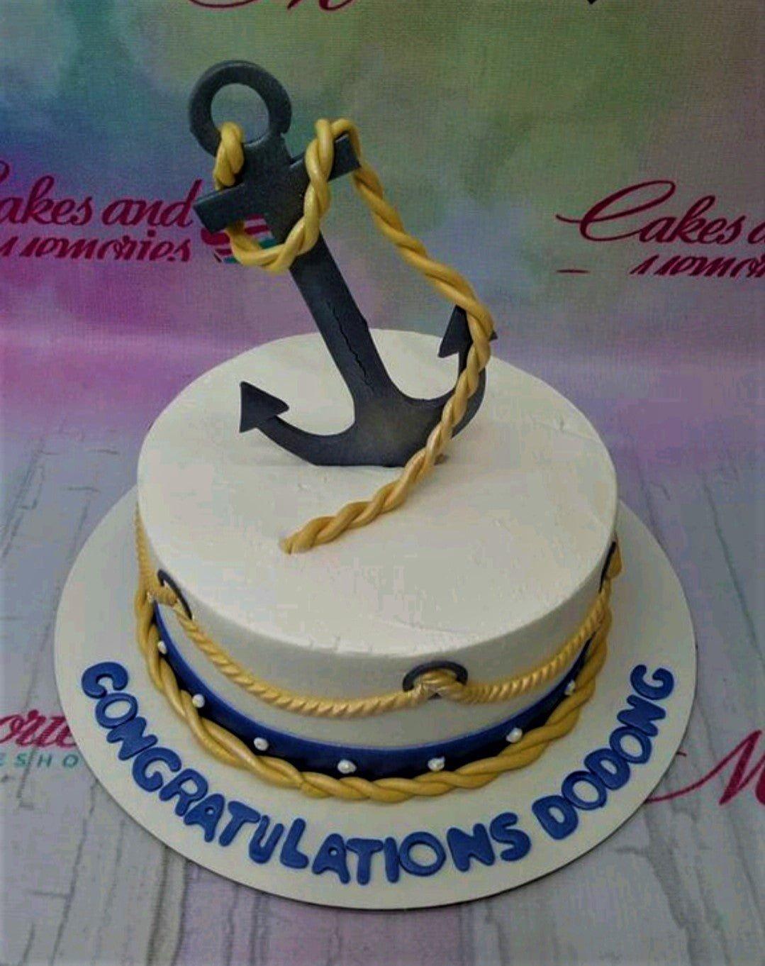 White nautical themed cake with a large black anchor topper and gold rope icing details.