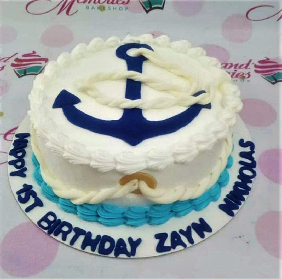 Nautical themed 1st birthday cake with a large blue anchor and white rope icing decorations on a white base with blue borders.