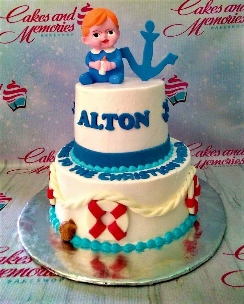 Two-tier nautical themed baptism cake in white and blue with a fondant baby figure, anchor, and lifebuoy decorations.