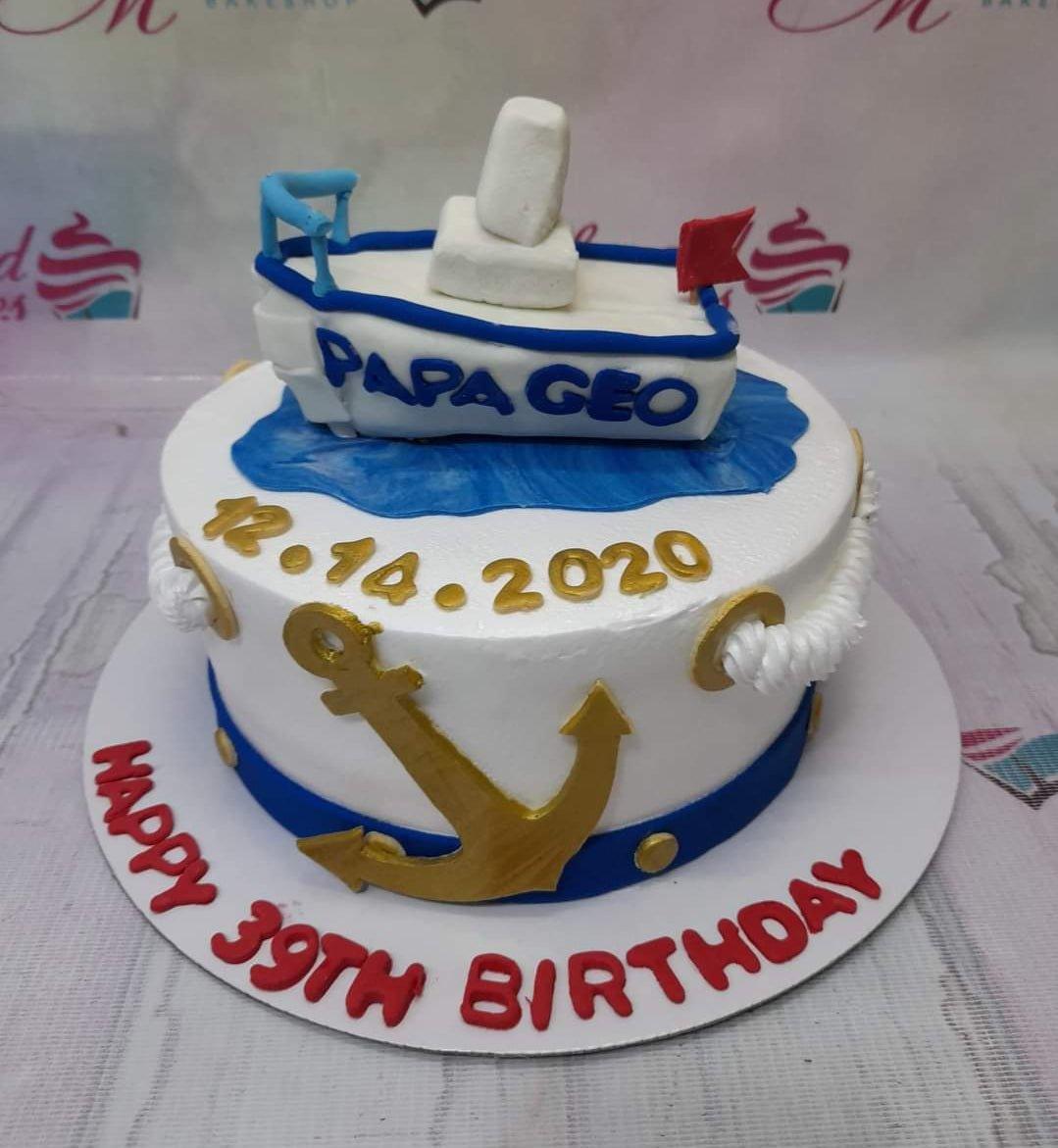 Nautical themed white fondant cake with a 3D fondant boat topper, gold anchor, and blue wave accents for a 39th birthday.