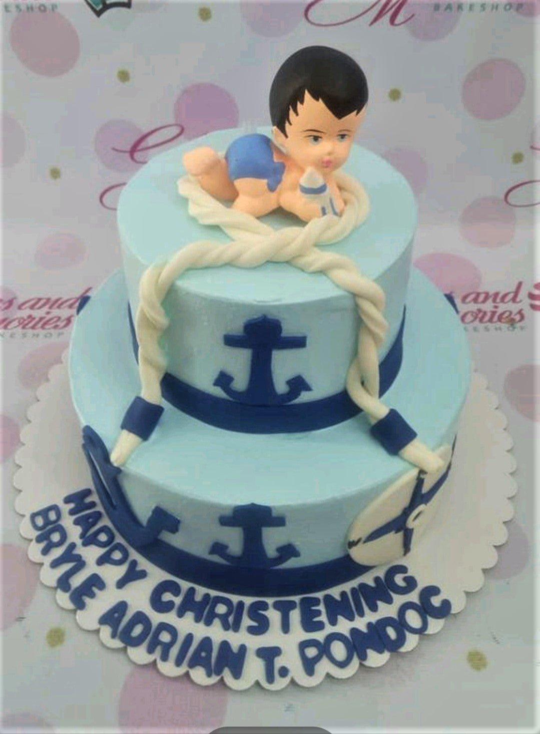 Two-tier light blue nautical themed christening cake with a 3D baby figure, anchors, and rope decorations.