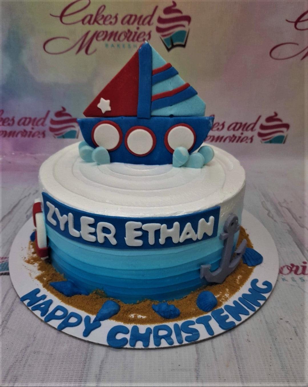Blue and white nautical themed christening cake with a 3D fondant boat topper, anchor, and lifebuoy decorations.