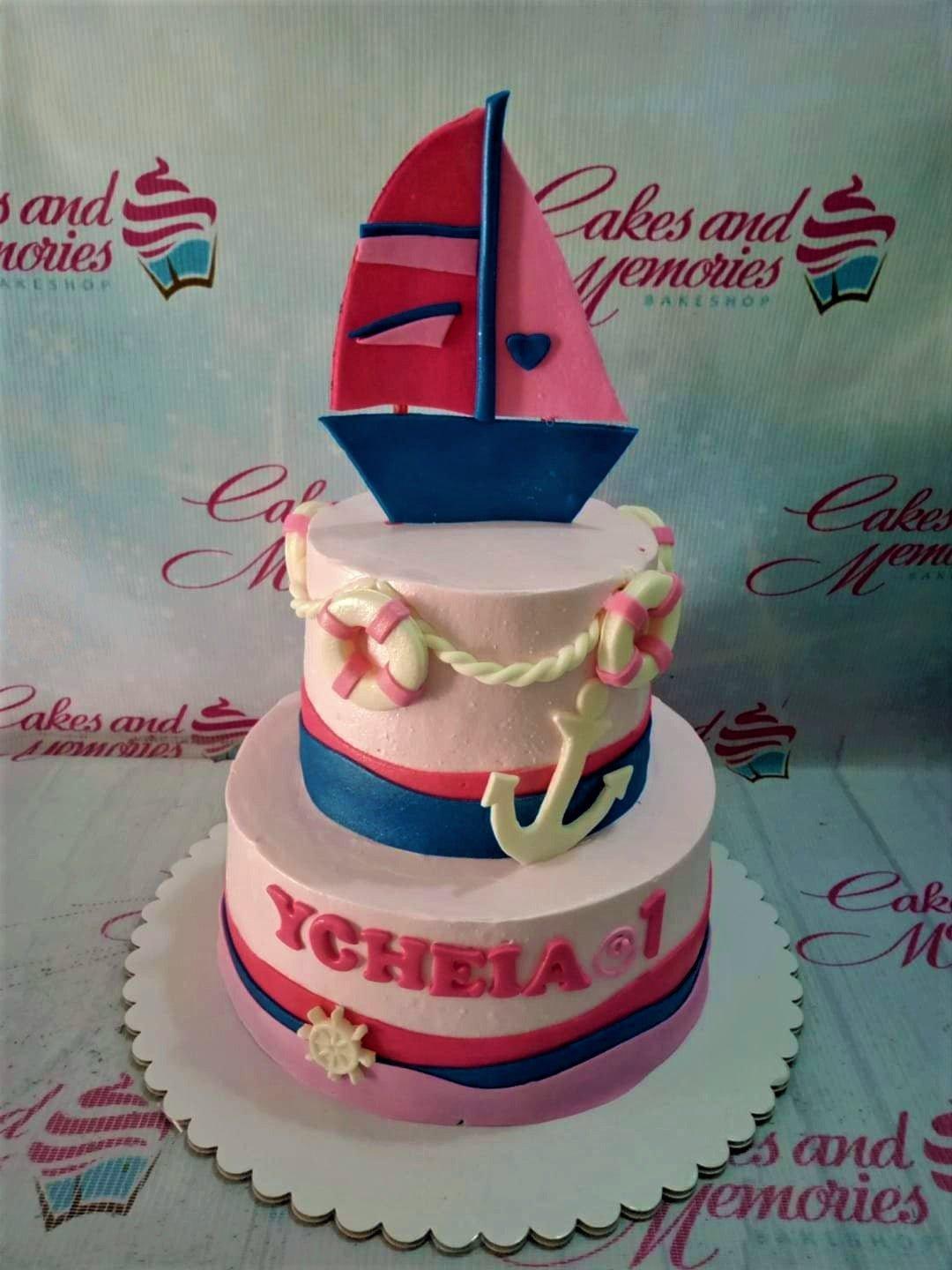 Pink 2-tier nautical themed birthday cake with a large fondant sailboat topper, anchors, and lifebuoys.