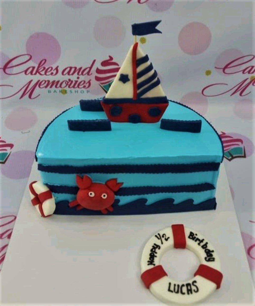 Nautical themed half-circle cake in light blue with a fondant sailboat topper, red crab, and lifebuoy message board.