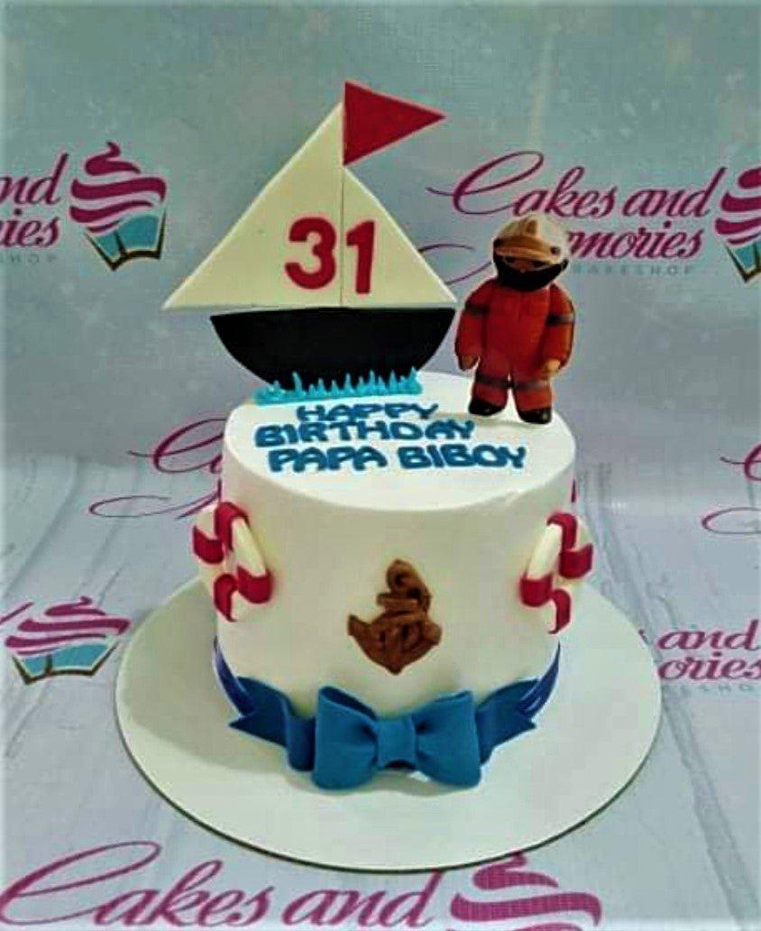 Nautical themed birthday cake for Papa Biboy featuring a fondant sailor figure, a sailboat topper with the number 31, and lifebuoy accents.