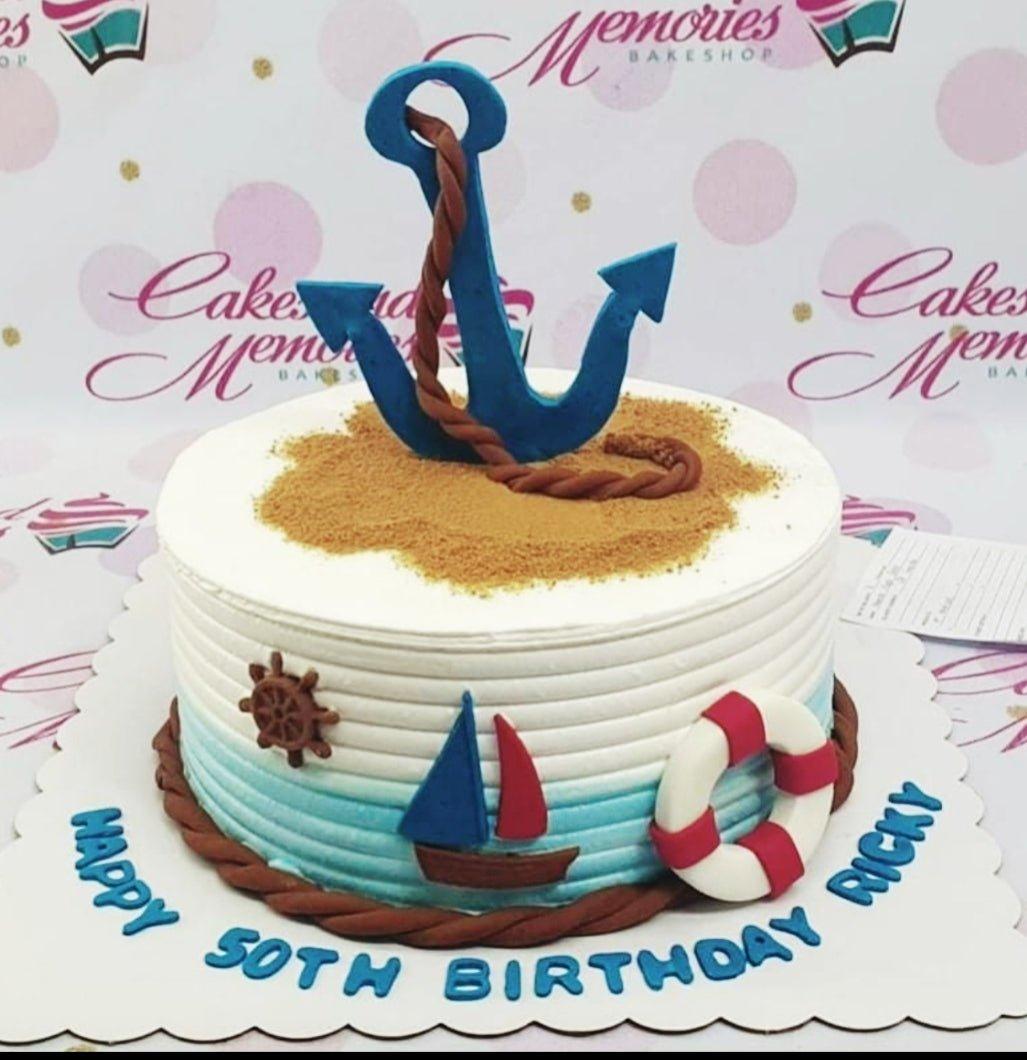 Nautical themed 1-tier birthday cake with a large blue anchor, brown rope, and sailboat decorations on white and light blue gradient icing.