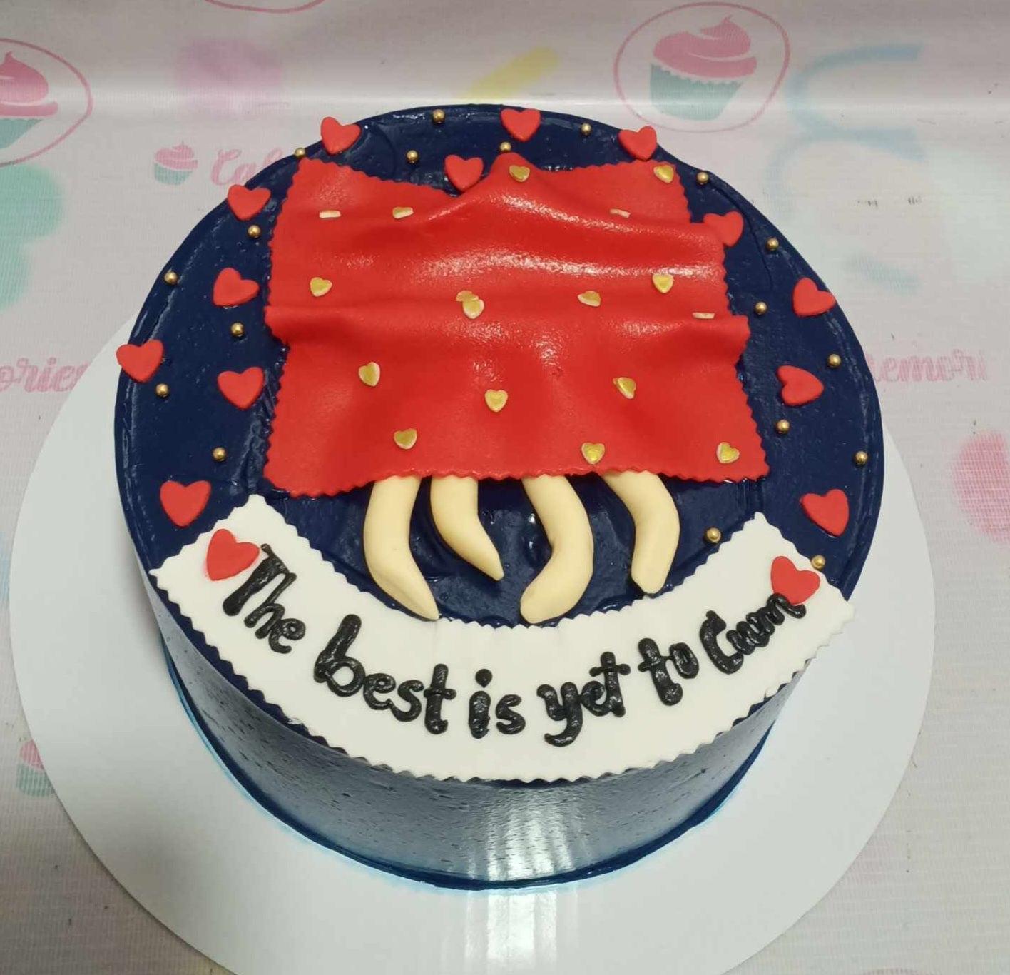Navy blue round cake with a red fondant blanket topper, small red hearts, gold beads, and a white banner message.