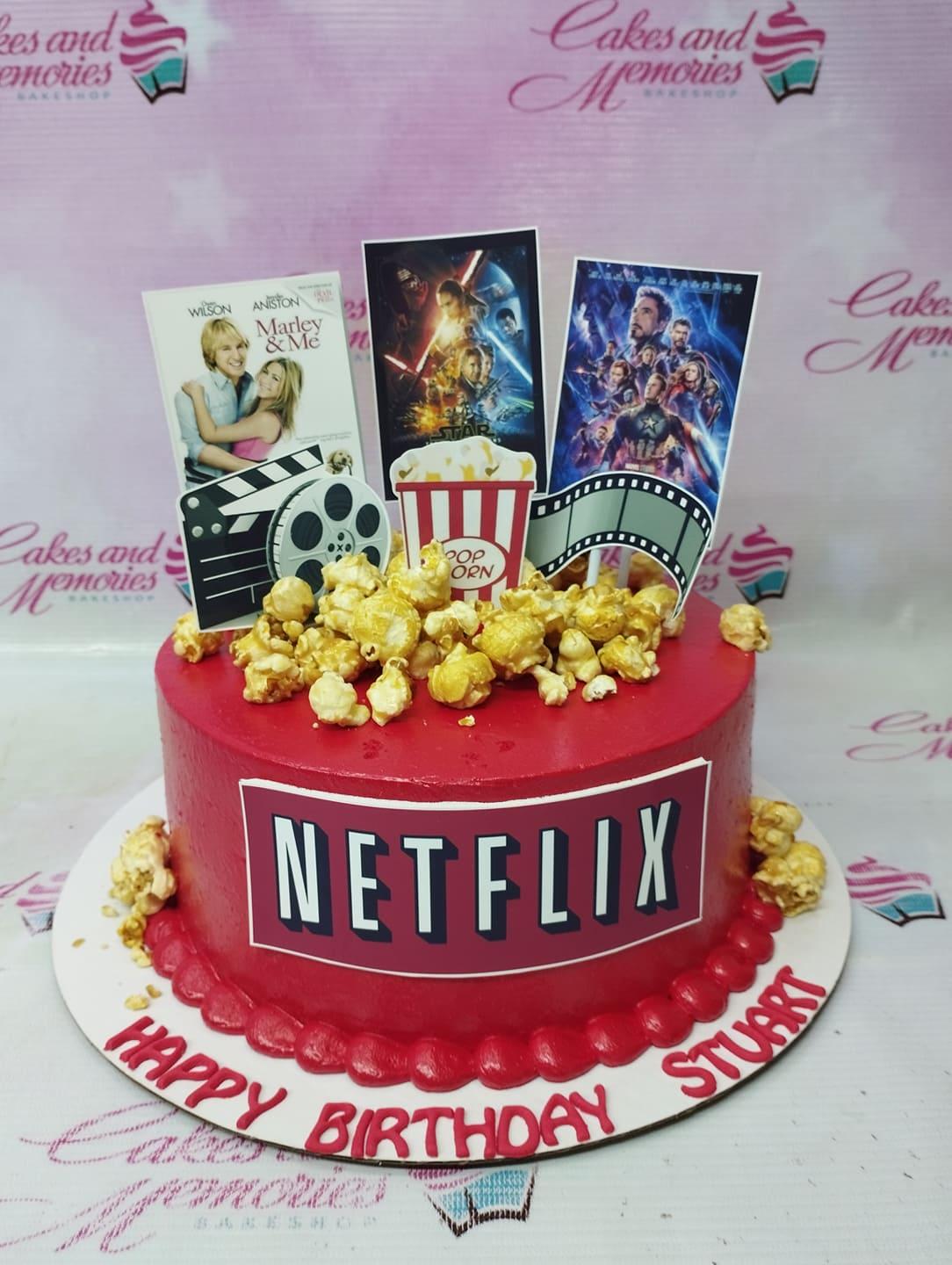 Red Netflix themed birthday cake with popcorn, movie posters, and film reel toppers for Stuart.