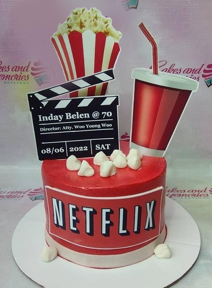 Red Netflix themed birthday cake with popcorn, soda, and movie clapperboard toppers for a 70th birthday celebration.