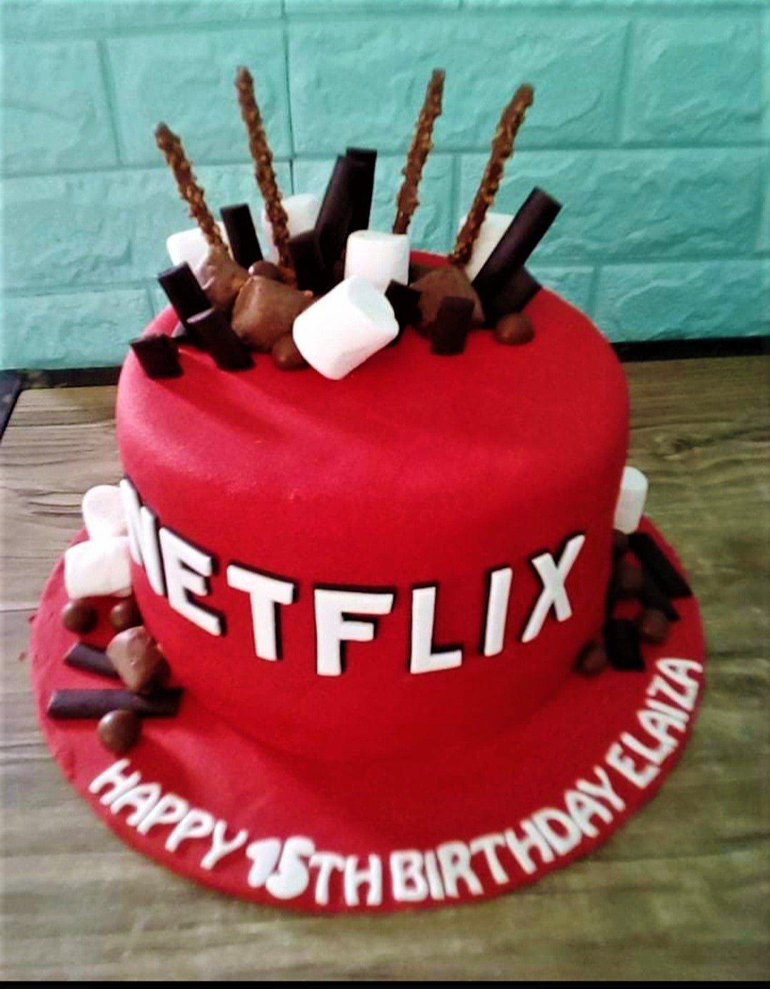 Red Netflix themed fondant cake with chocolate sticks, marshmallows, and chocolate pieces on top and base.