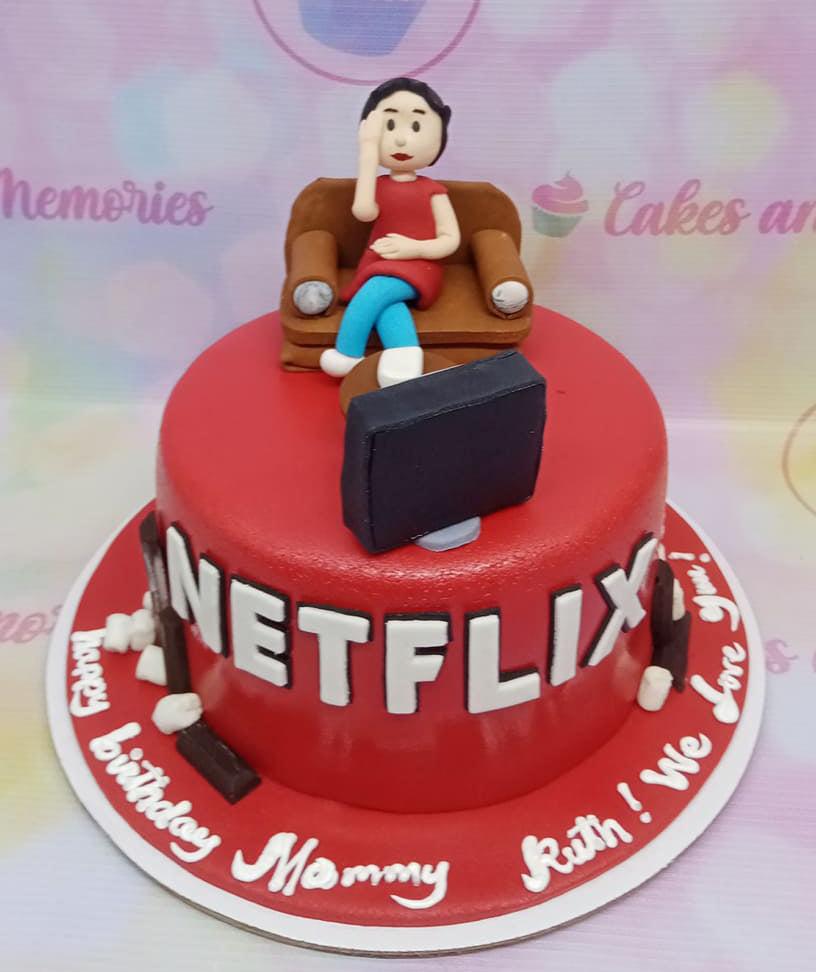 Red Netflix themed birthday cake with a fondant woman sitting on a sofa watching a TV topper and white Netflix logo on the side.