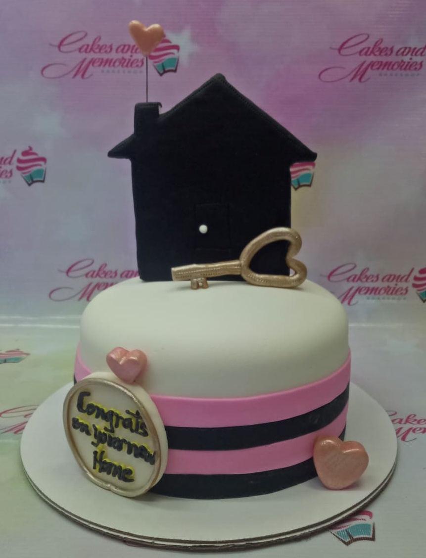 White fondant cake with black and pink stripes, featuring a black house topper, a gold key, and rose gold hearts.