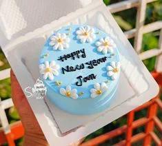 Light blue bento cake decorated with white icing daisies and a Happy New Year message in black icing.