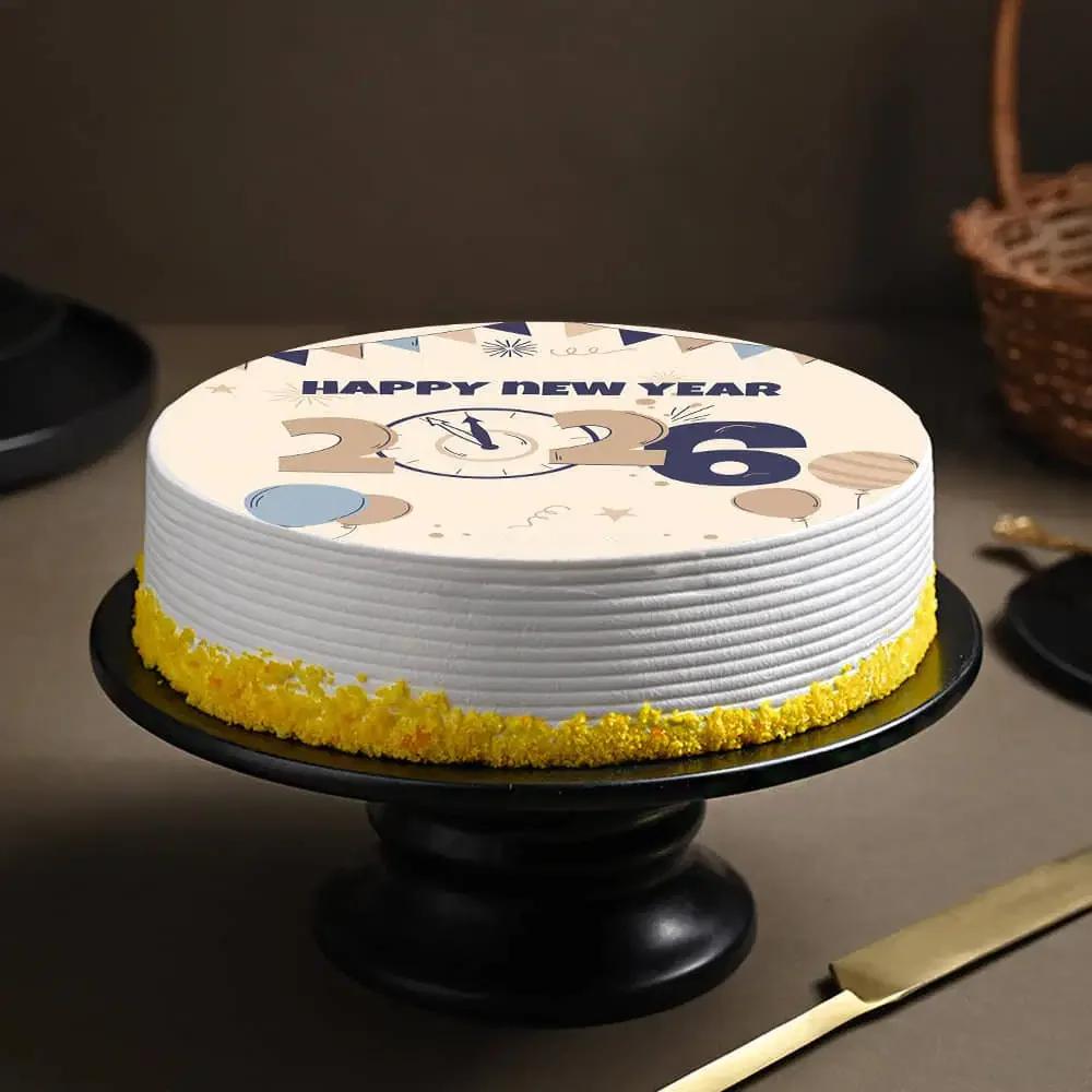 White round New Year 2026 cake with a printed clock and balloon design on top and yellow icing at the base.