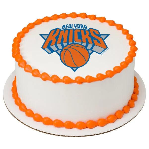 White round cake with orange piped borders and a New York Knicks logo printout on top.