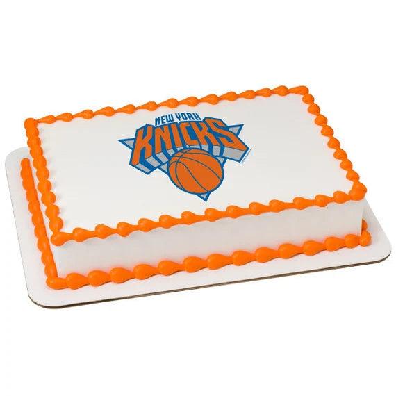 Rectangle white cake with orange piped icing borders and a New York Knicks basketball logo printout in the center.