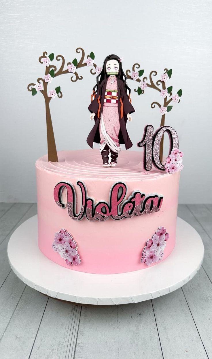 A pink 1 tier cake featuring a Nezuko Kamado character, a number 10 topper, cherry blossom trees, and cherry blossom flowers.